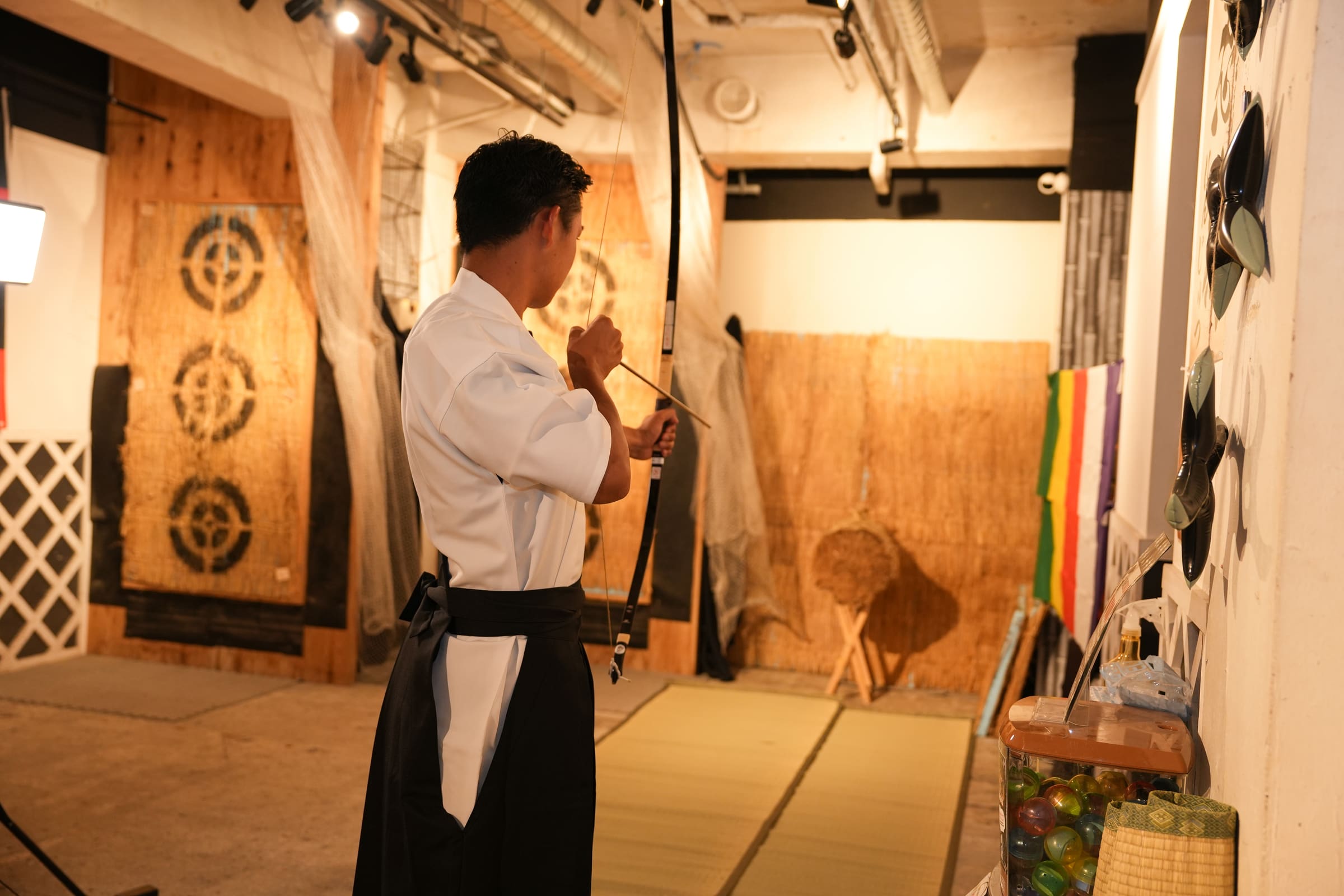 Guest in hakama nocking an arrow toward a straw target at an indoor kyudo Japanese archery range