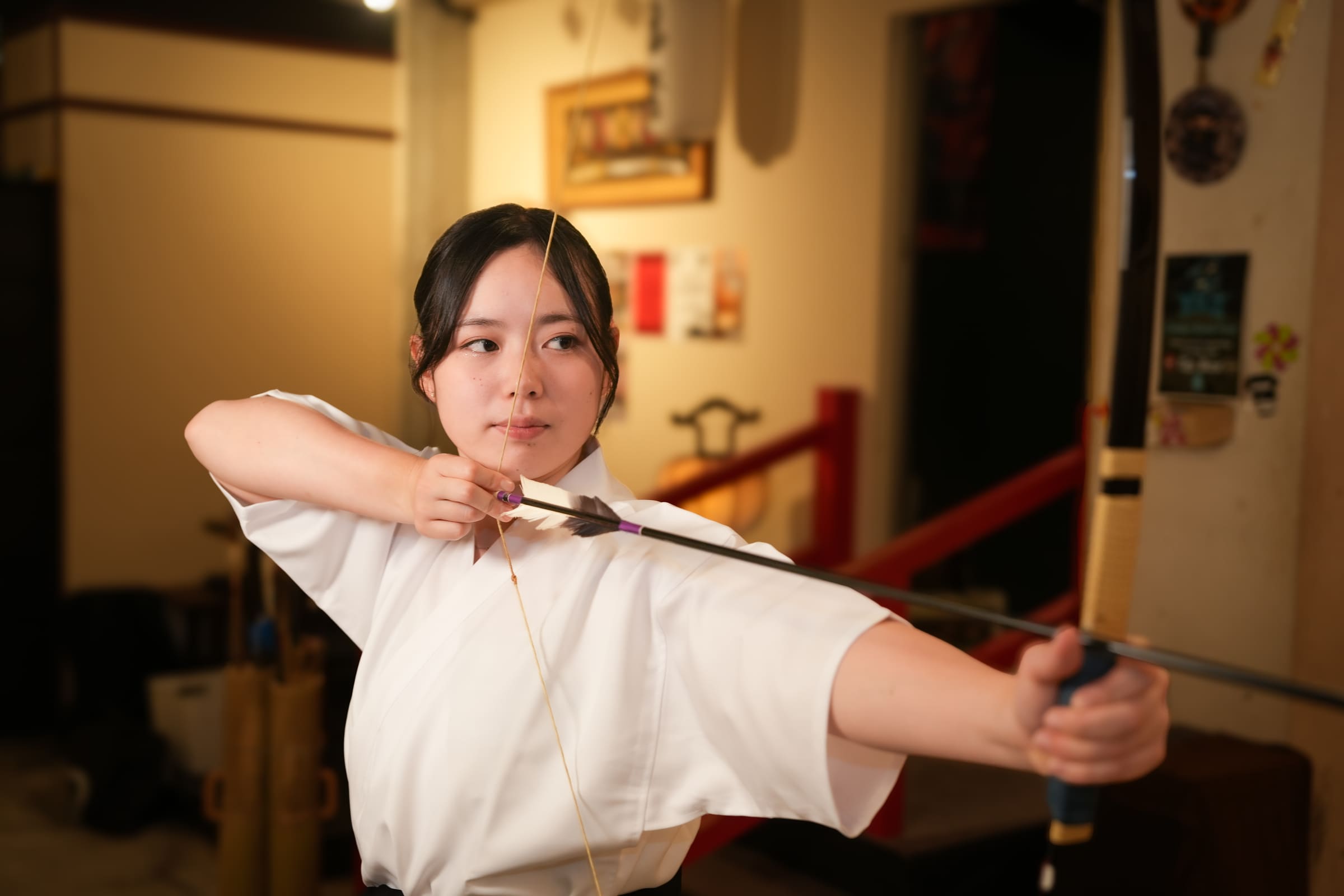 Woman in white keikogi drawing a Japanese archery bow with focused concentration during a kyudo experience