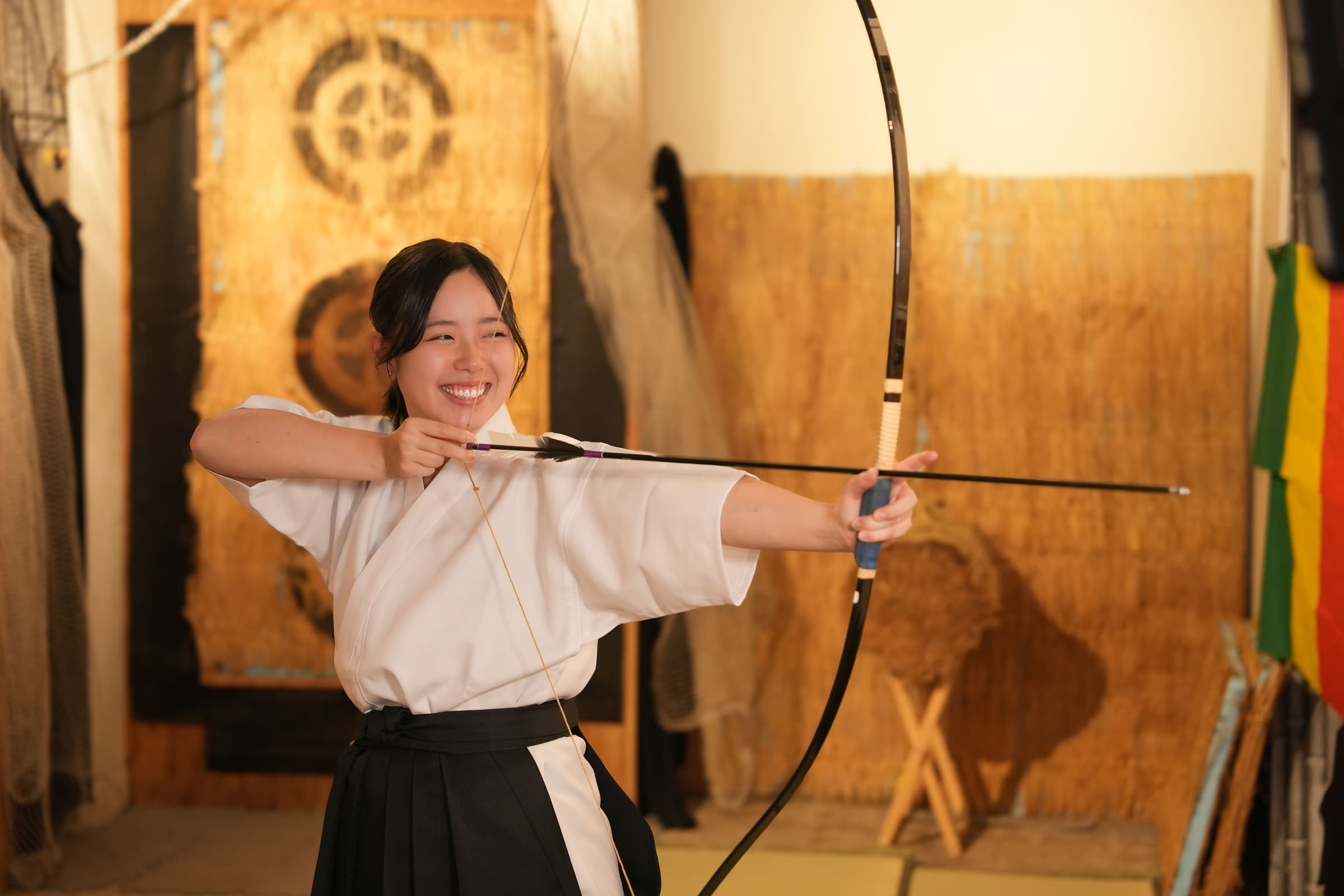 Joyful woman in black hakama at full draw with a Japanese archery bow during a fun kyudo experience