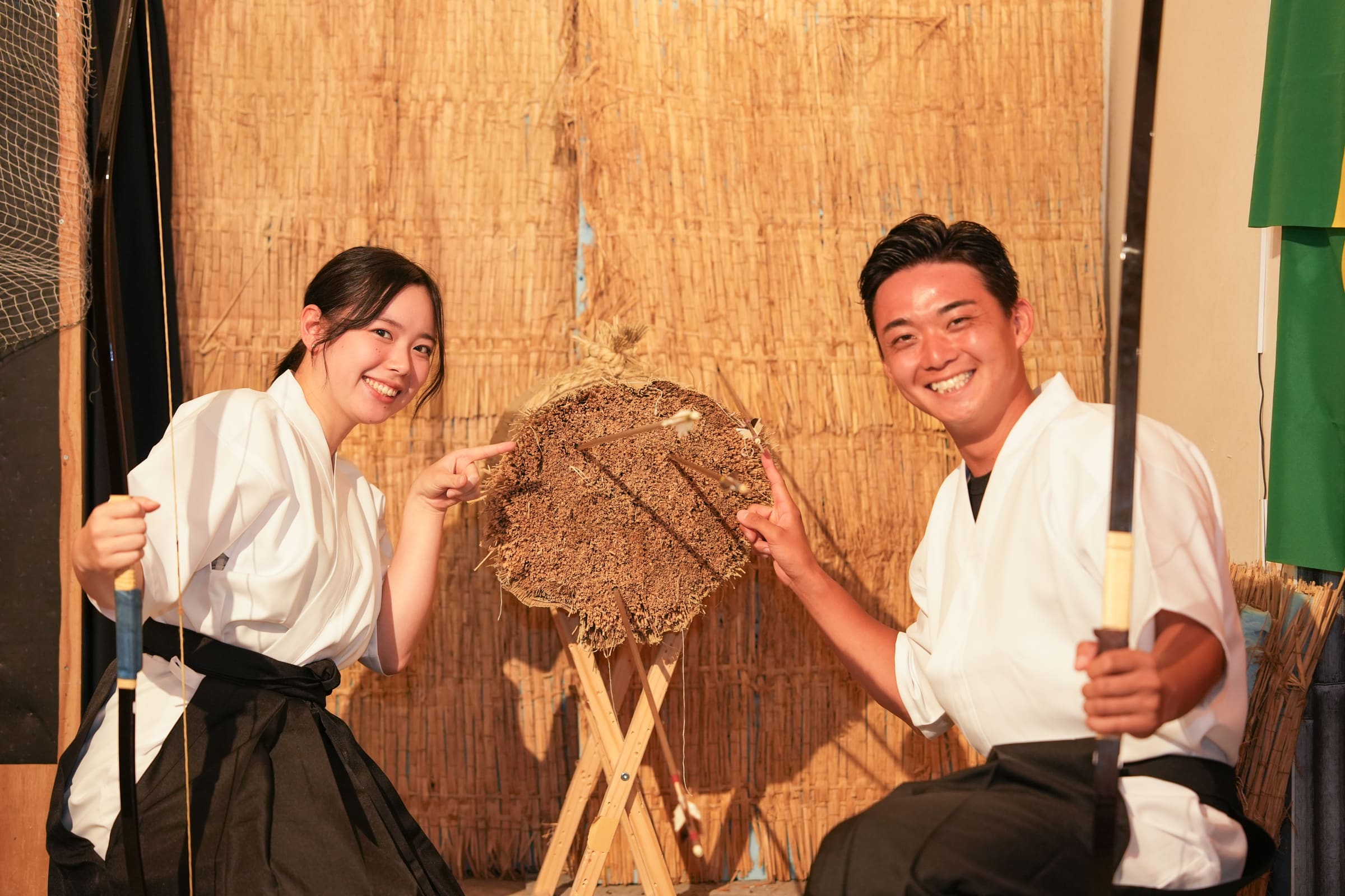 Two smiling friends in hakama pointing at arrows in a straw target after a kyudo Japanese archery experience