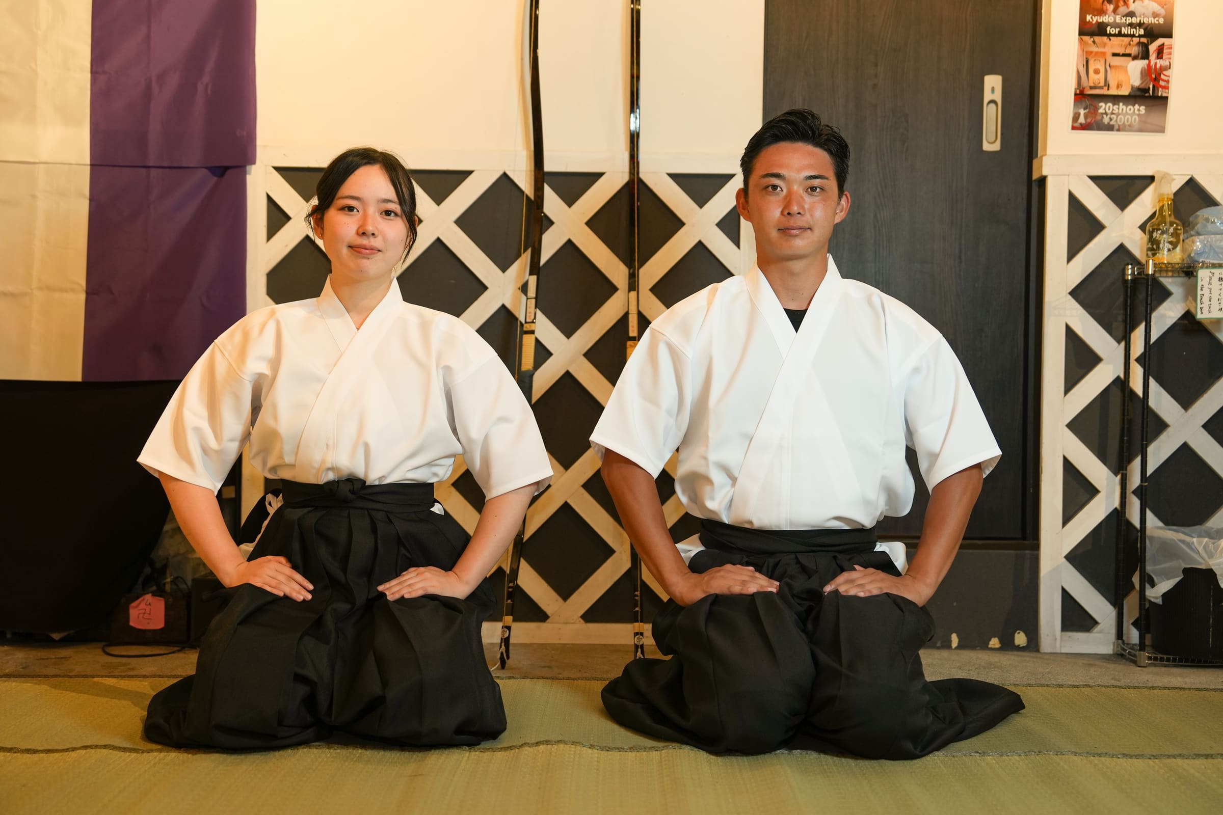 Two participants in white keikogi and black hakama kneeling in seiza before a kyudo Japanese archery lesson