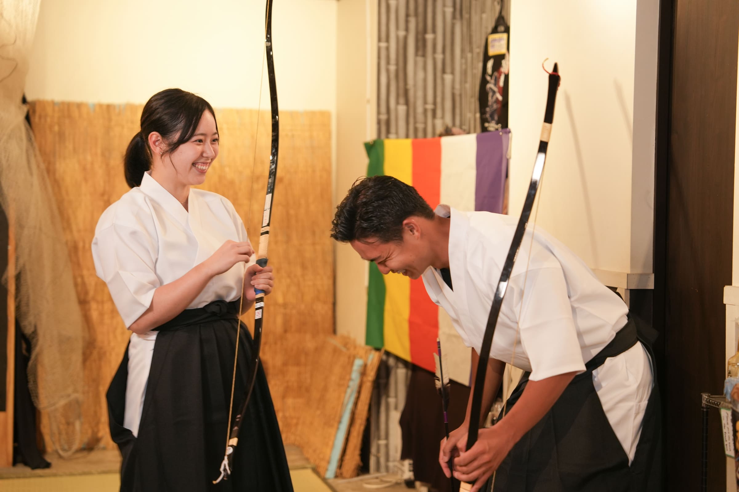 Friends in hakama sharing a laugh with Japanese longbows during a casual kyudo archery experience