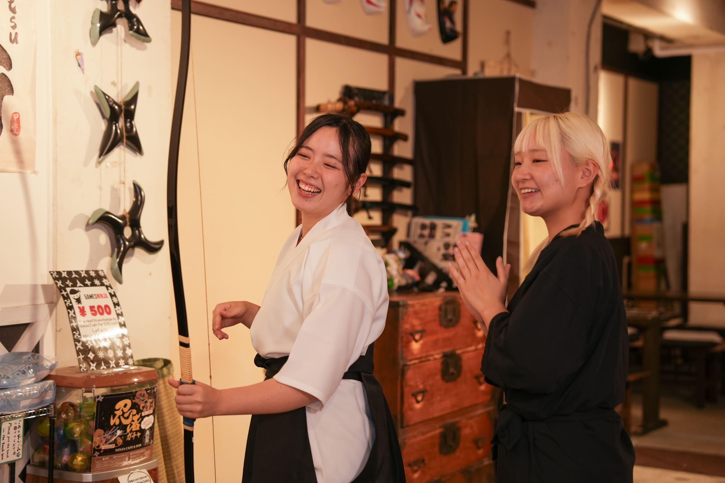 Smiling guest in hakama holding a kyudo bow as her instructor applauds during a Japanese archery experience