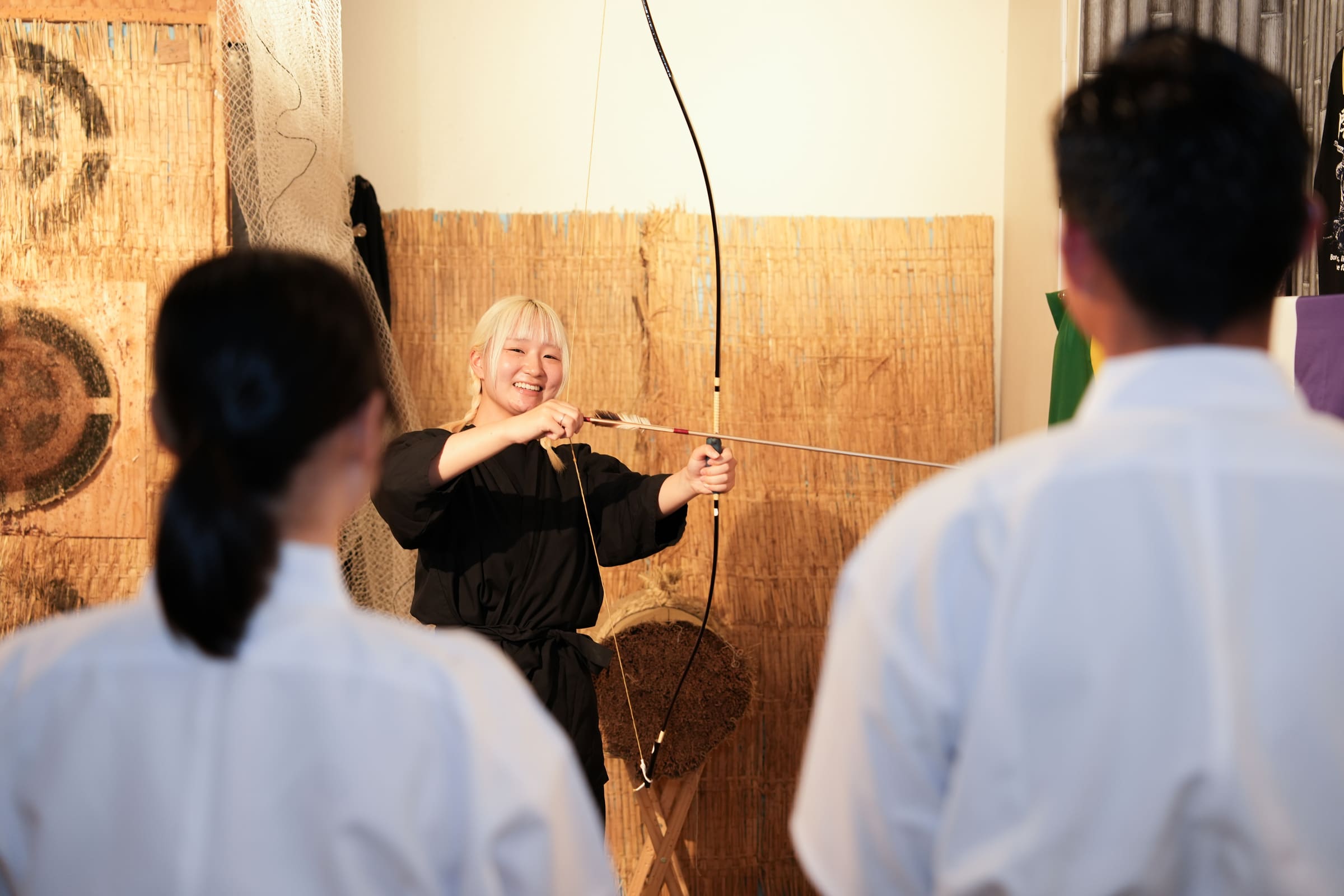 Kyudo instructor demonstrating how to nock an arrow on a Japanese bow as two guests watch during a lesson